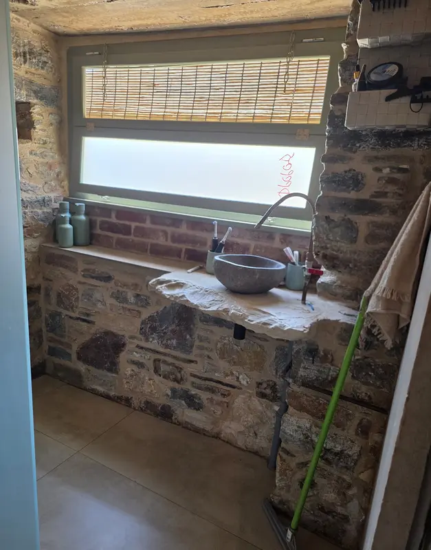 Badkamer met stenen wasbak op een natuurstenen bank onder het raam